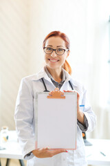 Woman-doctor standing and showing empty medication history record form in hospital or clinic 