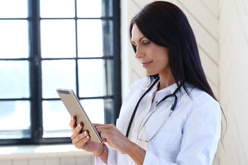 Image of a professional, confident female doctor with stethoscope holding a digital tablet at...