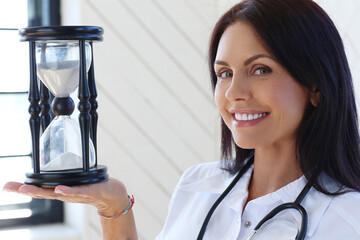 Professional,confident,smiling female-doctor with stethoscope holding an hourglass.