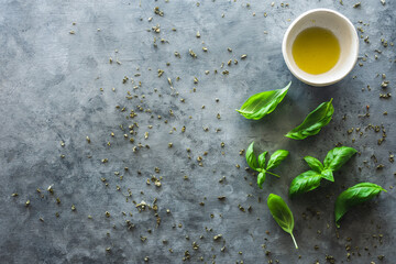 vista superior de hojas de albahaca y un bol con aceite de oliva, sobre fondo gris, con espacio en...