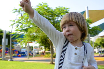 A little boy in a white shirt and striped suspenders makes faces. Football fan. Funny naughty kid....