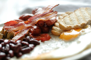 Side view of English breakfast with fried eggs, bacon,bread and vegetables in white plate.