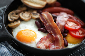 Close view of English breakfast with fried eggs, bacon,sausages, bread and vegetables in pan.