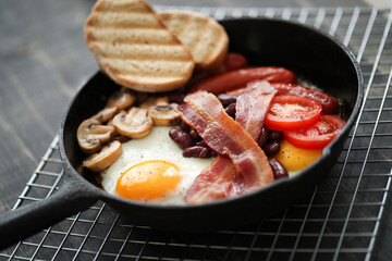 Close view of English breakfast with fried eggs, bacon,sausages, bread and vegetables in pan.