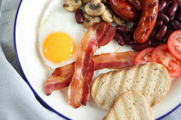 Close view of English breakfast with fried eggs, bacon,sausages, bread and vegetables in white plate.