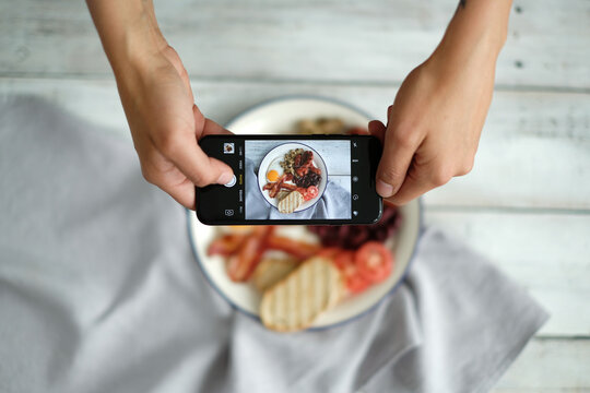 Top view of man`s hands taking picture of English breakfast with fried eggs, bacon,bread and vegetables in white plate.