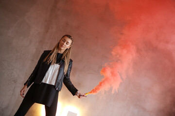 Stock photo of a dreadlocks girl holding a smoke bomb that throws red smoke around. 