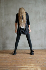 Full-size photo of a young woman with dreadlocks wearing oversize shirt standing and posing against stone background.