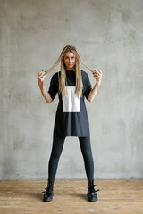 Fototapeta premium Full-size photo of a young woman with dreadlocks wearing oversize shirt standing and posing against stone background.