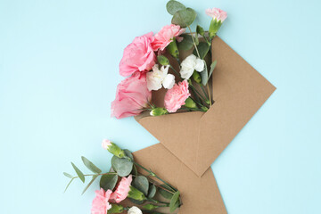 Top view of pink, beautiful flowers in craft envelopes on a blue background.