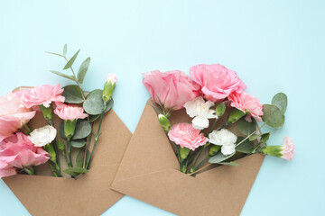 Top view of pink, beautiful flowers in craft envelopes on a blue background.