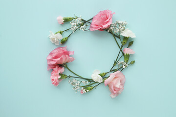 Top view of circle of beautiful, pink flowers with leaves on a blue surface.