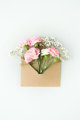 Top view of pink, beautiful flowers in craft envelopes on a white background.