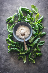 cuenco con sal y una cuchara, rodeado de hojas de albahaca, sobre fondo gris
