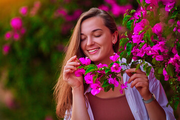 Portrait of a happy cute smiling caucasian girl with closed eyes and a branch of pink flowers in the garden outdoors