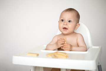 A cute little baby sits in a high chair and plays educational games. wooden construction set. Ecological. A light background, a place for text.