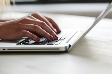 Women’s hands typing text on the computer on the table.