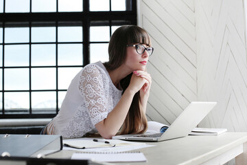 Young, beautiful, cute girl with bangs in glasses studying on the computer against windowsill.