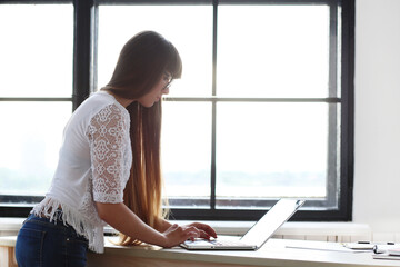 Young, beautiful, cute girl with bangs in glasses studying on the computer against windowsill.