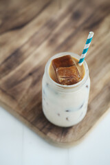 Top view of glass of a iced coffee with cream milk and straw on wooden surface.