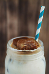 Cropped view of glass of a iced coffee with cream milk and straw on wooden surface.