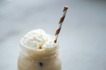A glass cup of iced coffee with whipped cream on top and straw 