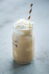 A glass cup of iced coffee with whipped cream on top and straw 