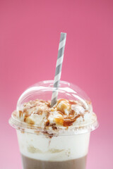 Close view of a tasty caramel milkshake with straw on a pink background.