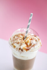 Close view of a tasty caramel milkshake with straw on a pink background.