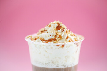 Close view of a tasty caramel milkshake on a pink background.