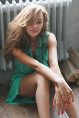 Naklejka premium Close-up portrait of a beautiful,young,relaxed lady in green dress sitting on the wooden floor.