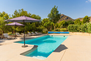 Swimming pool with umbrellas in a country house on a sunny day surrounded by nature and mountains