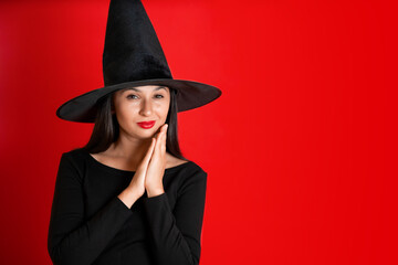 Halloween. A young beautiful woman in a witch's hat and a black dress on a red colored background. Space for text.