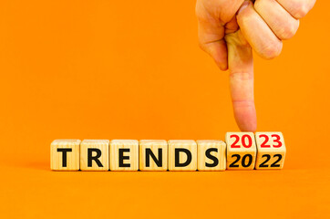 2023 trends new year symbol. Businessman turns a wooden cube and changes words Trends 2022 to Trends 2023. Beautiful orange table orange background, copy space. Business 2023 trends new year concept.