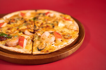 Close up slice of tasty hot baked seafood crispy pizza - mussels, shrimps and kani (crab stick), chili pepper and melted mozzarella cheese on a wooden pizza pan over the red background.