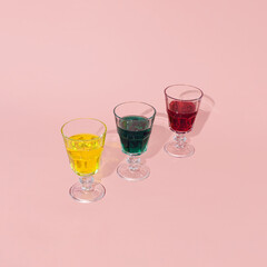 Three vintage style wine glasses, colored drinks, creative arrangement on pastel pink background. Holidays celebration. 