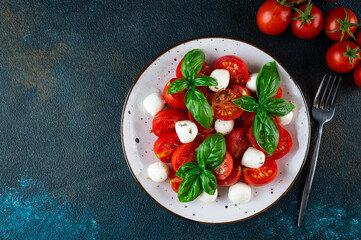 Italian caprese salad with sliced tomatoes, mozzarella, basil, olive oil on a dark background. Top view. Italian food. Healthy salad. Summer food