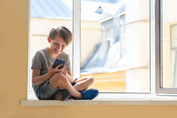a smiling little boy sits on the windowsill by the open window, the child communicates by video link