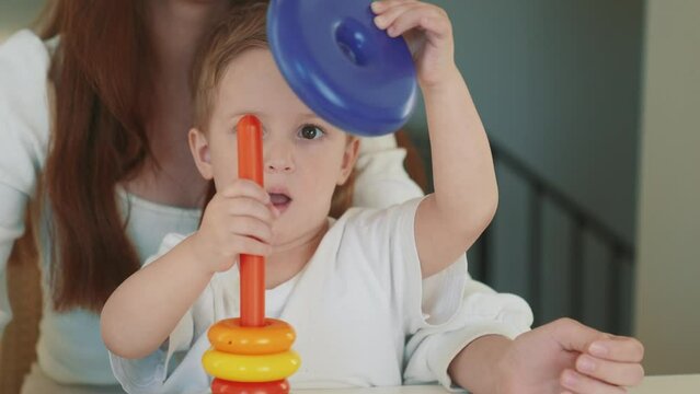 the child collects a toy pyramid. mom plays with son at home happy family. development of fine motor skills in fun a newborn child. happy family mom and baby play pyramid game. preschool education
