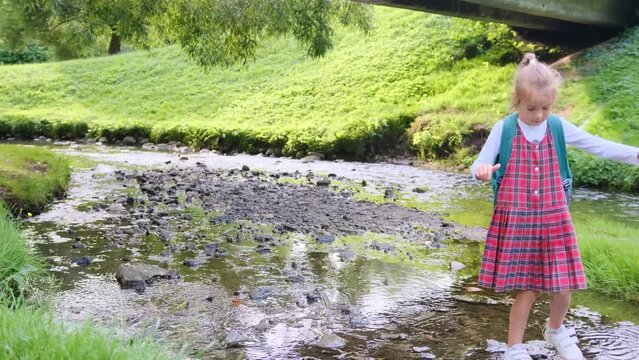 a schoolgirl girl crosses a stream stepping on stones.