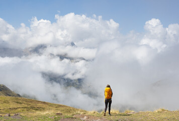 Girl with yellow backpack hiking in the Pyrenees, with the mountains in the clouds in the background.
