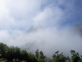Obraz na płótnie Canvas Paisaje con nubes bajas de niebla blanca tapando montañas, y árboles verdes, en verano 2021