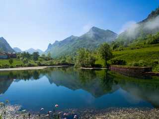 Vistas de un lago con las montañas reflejadas en el agua azul y árboles verdes en la zona de...
