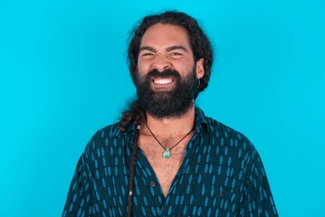 Mad crazy young bearded man wearing blue shirt over blue studio background clenches teeth angrily, being annoyed with coming noise. Negative feeling concept.