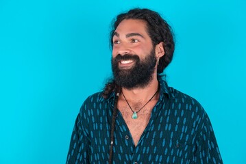 Fototapeta premium Oops! Portrait of young bearded man wearing blue shirt over blue studio background clenches teeth and looks confusedly aside, realizes her bad mistake,