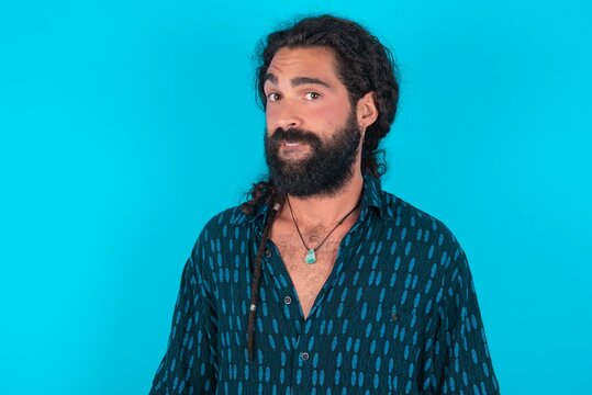 young bearded man wearing blue shirt over blue studio background being nervous and scared biting lips looking camera with impatient expression, pensive.