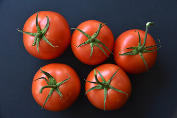 Several delicious red tomatoes in a row on a black background. Juicy red tomatoes close-up.