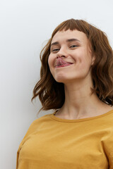 horizontal close-up portrait of a beautiful, playful, tanned woman in a yellow T-shirt on a light background amusingly showing her tongue to the camera smiling broadly