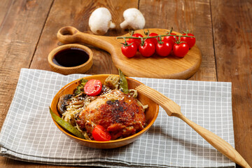 Udon with vegetables and chicken on the table in a wooden plate next to champignons and tomatoes on...
