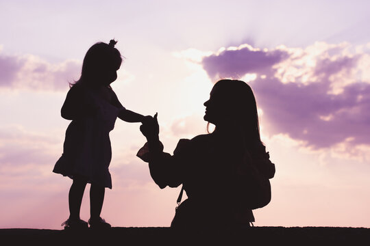 A mom, mother holding by the hand a little daughter against a pink sky. Two contrasting figures silhouettes. Interaction of parents children. Psychology of parenting a child, kid. Reproductive Clinic.